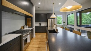 Una cocina moderna con una isla central, electrodomésticos de acero inoxidable y grandes ventanas con vistas a zonas verdes.