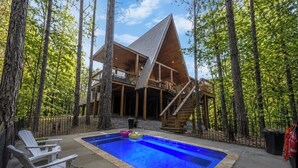 Una cabaña de madera con piscina, rodeada de árboles.