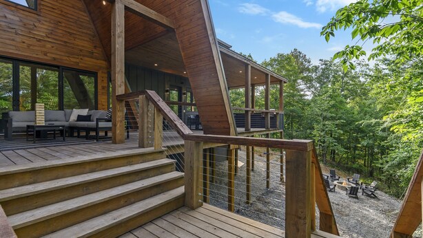 Una terraza de madera con mobiliario exterior, una escalera y vistas a un área boscosa.