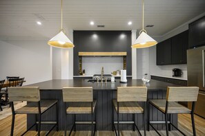 Une cuisine moderne dotée d’un îlot central, de luminaires suspendus et de meubles de couleur sombre.