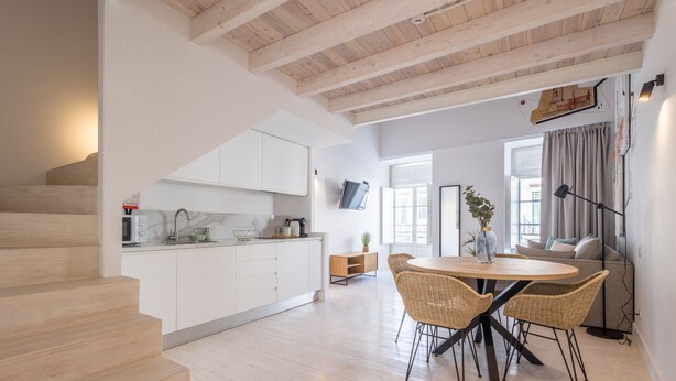 A modern kitchen with white cabinets, a dining area with wicker chairs, and a staircase. - Suits Boutique Arco - Mezanino apartment by HD (Faro)