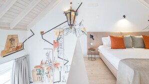 A bedroom with a sloped ceiling, a bed with multiple pillows, a hanging light fixture, and wall art depicting architectural drawings. - Suits Boutique Arco - Mezanino apartment by HD (Faro)