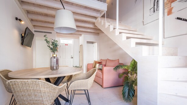 Un interno moderno con un tavolo da pranzo in legno, sedie in vimini, un divano rosa e una scala.