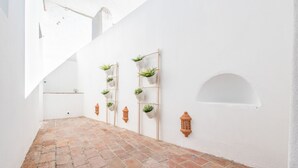 Un corridoio stretto con piastrelle in terracotta, pareti bianche e lanterne in terracotta.