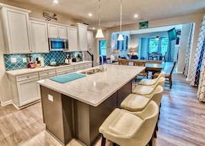 A kitchen with a central island, bar stools, a microwave, and a dining area with a table and chairs.