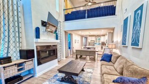 A spacious living room with a fireplace, a dining area, and a kitchen in the background.
