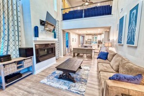 A spacious living room with a fireplace, a dining area, and a kitchen in the background. - Bayside * 4BR Luxury Twinhouse (Selbyville)