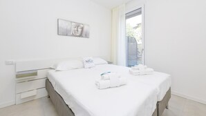 A modern hotel room with a large bed, a bedside table, a wall-mounted artwork, and a view through a window.
