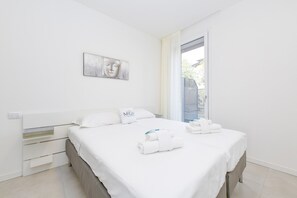 A modern hotel room with a large bed, a bedside table, a wall-mounted artwork, and a view through a window.