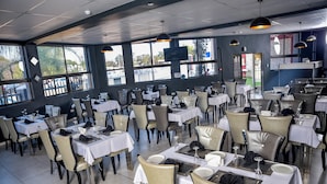 Een restaurant met meerdere tafels en stoelen, grote ramen en een modern interieur.
