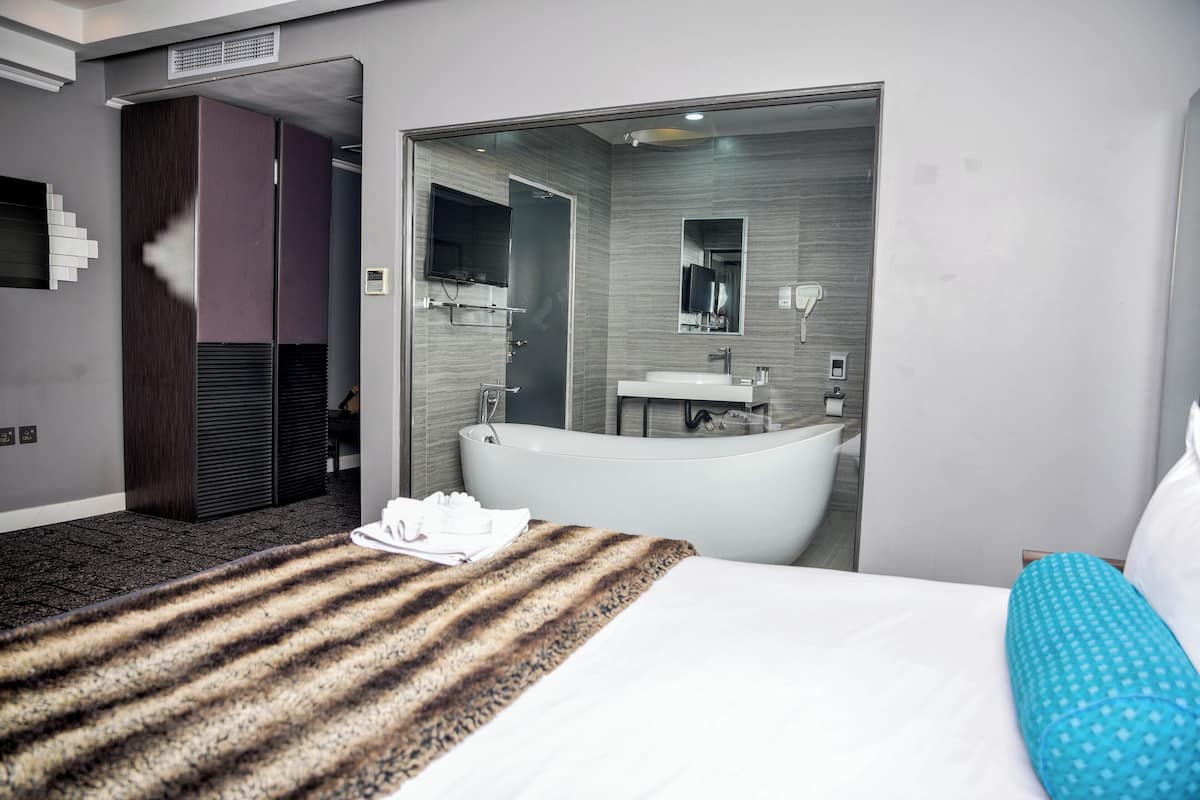 A modern hotel room with a large bed, a separate bathroom with a bathtub, and a wardrobe.