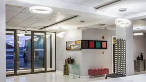 Een moderne lobby met glazen deuren, een receptiebalie en moderne verlichtingsarmaturen.