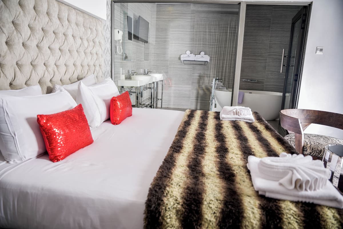 A hotel room with a large bed, a bathroom with a glass shower, and a view of the city.