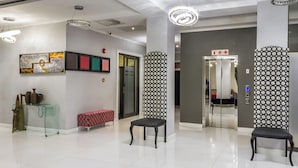 Een moderne lobby met een glazen tafel, een bank, een wand met patroon en een plafond met inbouwverlichting.