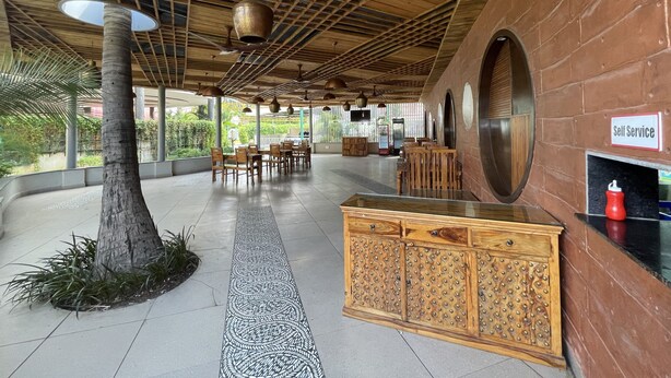 A spacious lobby with a wooden ceiling, a central tree, and a self-service kiosk. - Hotel Kanha's Palm Springs (Bhopal)