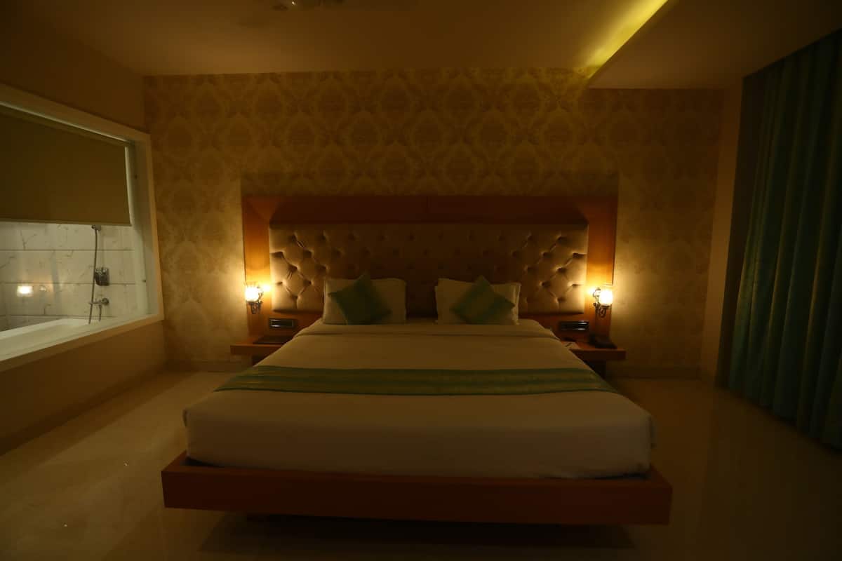 Une chambre à coucher moderne avec un grand lit, deux tables de chevet avec des lampes, une tête de lit à motifs capitonnés et une fenêtre donnant sur l’extérieur.