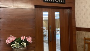 A wooden door with a sign reading "Suroor" and a small table with a floral arrangement beside it. - Hotel Kanha's Palm Springs (Bhopal)