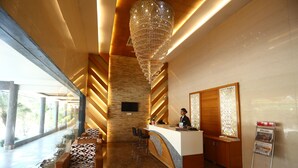 A reception area with a receptionist desk, seating, and a large chandelier. - Hotel Kanha's Palm Springs (Bhopal)