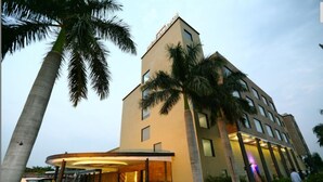 A modern hotel with a curved entrance, palm trees, and a car parked in front. - Hotel Kanha's Palm Springs (Bhopal)