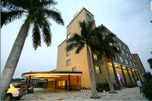 A modern hotel with a curved entrance, palm trees, and a car parked in front. - Hotel Kanha's Palm Springs (Bhopal)