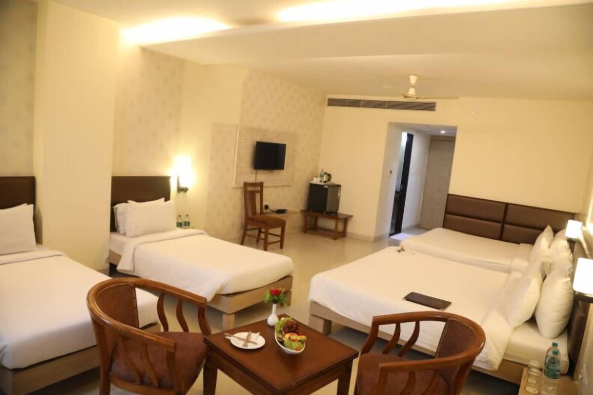 Une chambre d’hôtel avec deux lits simples, un canapé-lit, une table à manger avec des chaises, une télévision et un petit bureau.