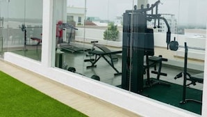Academia com equipamentos de ginástica, grandes janelas e vista para edifícios.