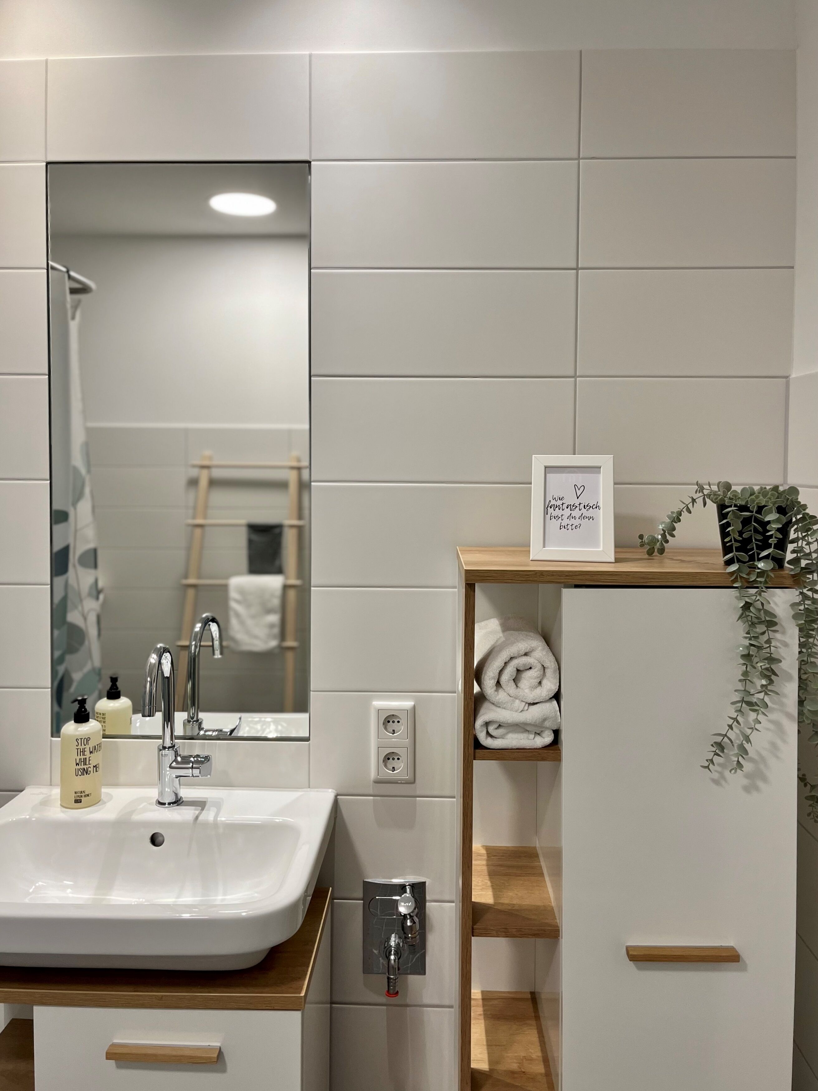 A modern bathroom with a white sink, a mirror, a towel rack, and a shelf with towels.