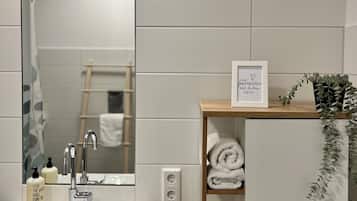 A modern bathroom with a white sink, a mirror, a towel rack, and a shelf with towels.