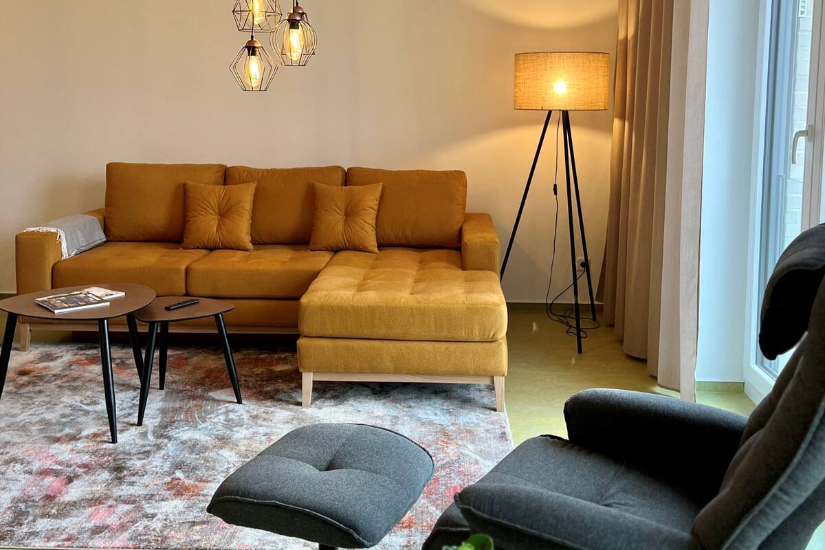 A living room with a mustard-colored sofa, a small round table, a floor lamp, and a grey armchair.