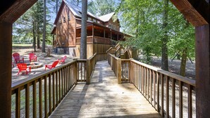 Une cabane en bois dotée d’une terrasse qui mène à un espace aménagé avec un foyer et des chaises rouges.