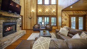 L’intérieur chaleureux d’un chalet avec une cheminée en pierre, des canapés en cuir et un grand téléviseur fixé au mur.