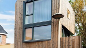 Een modern gebouw met een houten gevel, grote ramen en een fiets voor de deur.