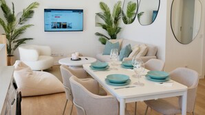 A modern living room with a white sofa, a dining table with teal plates, and a flat-screen TV mounted on the wall. - City Centre Ocean View Apartment (Lagos)