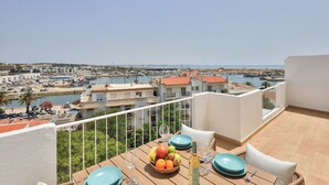 A balcony with a table set for dining, overlooking a marina and coastal town. - City Centre Ocean View Apartment (Lagos)