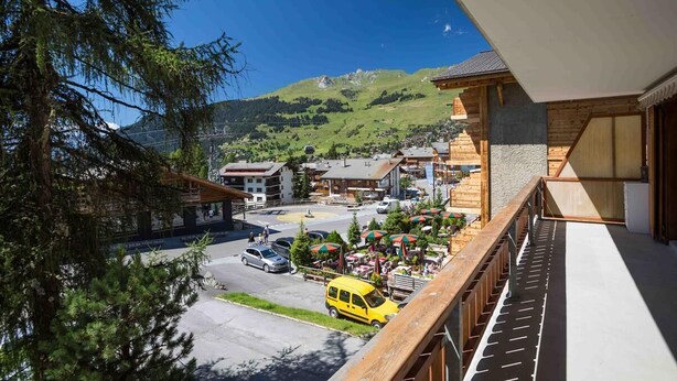 A mountain village with a wooden building, a parking area, and a yellow van. - Living room with eating area, kitchen with dishwasher, Nespresso machine and microwave, one bedroom (Verbier)