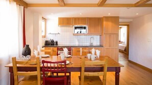 A kitchen with wooden cabinets, a built-in oven, and a dining area with a wooden table and chairs. - Living room with eating area, kitchen with dishwasher, Nespresso machine and microwave, one bedroom (Verbier)