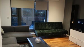 A modern living room with a dark grey sofa, a green velvet sofa, a wooden coffee table with a decorative vase, and a television on a white cabinet. - Immaculate 1-bed Apartment in London (London)