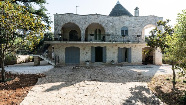 A stone building with a central courtyard, arched doorways, and a staircase leading to a balcony.