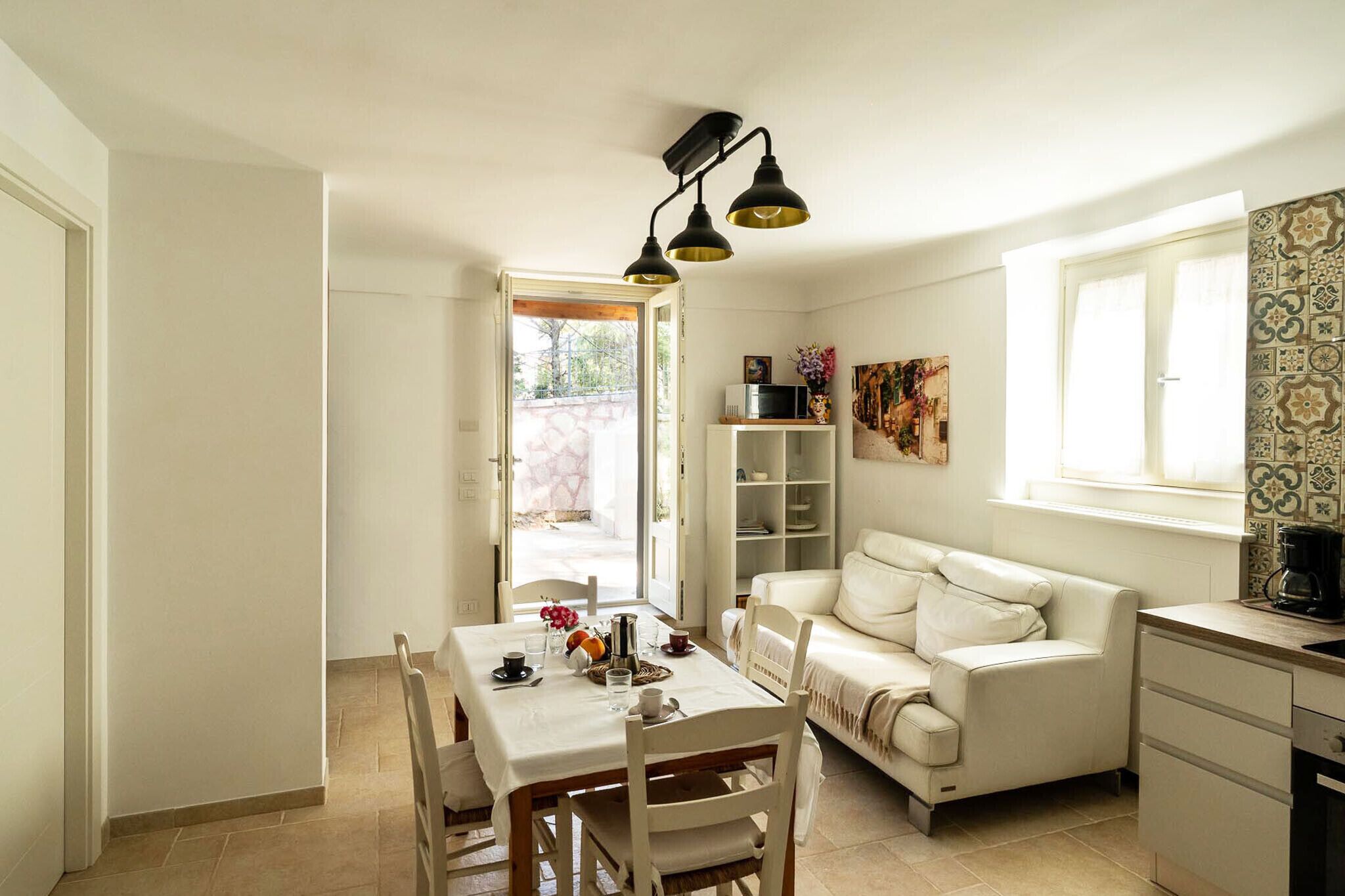 Un espace de vie compact comprenant un coin repas, un canapé, une cuisine et une fenêtre ornée de carreaux décoratifs.