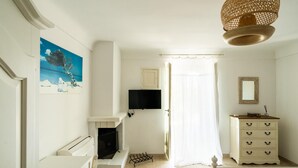 A room with a fireplace, a television, a dresser, and a painting on the wall.