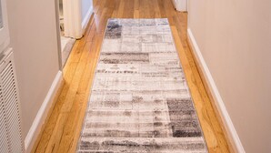 Un couloir au sol en bois, agrémenté d’un tapis à motifs, qui mène à une porte blanche au fond.