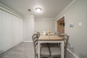 Comedor con mesa de madera y seis sillas, un jarrón con flores y una lámpara en el techo.