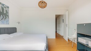 A bedroom with a bed, a wall-mounted lamp, a wicker ceiling light, a white chair, and a wardrobe. - Sixties 64 :  2 bedrooms apartment with a balcony and parking in Biarritz (Biarritz)