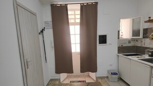 A kitchen with a tiled floor, a window with brown curtains, and a microwave. - Studio apartment in Sorrento Peninsula, 300 meters from the sea and free beach (Castellammare di Stabia)