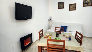 A dining area with a table set for four, a fireplace, a TV mounted on the wall, and a sofa with a blue pillow. - Studio apartment in Sorrento Peninsula, 300 meters from the sea and free beach (Castellammare di Stabia)