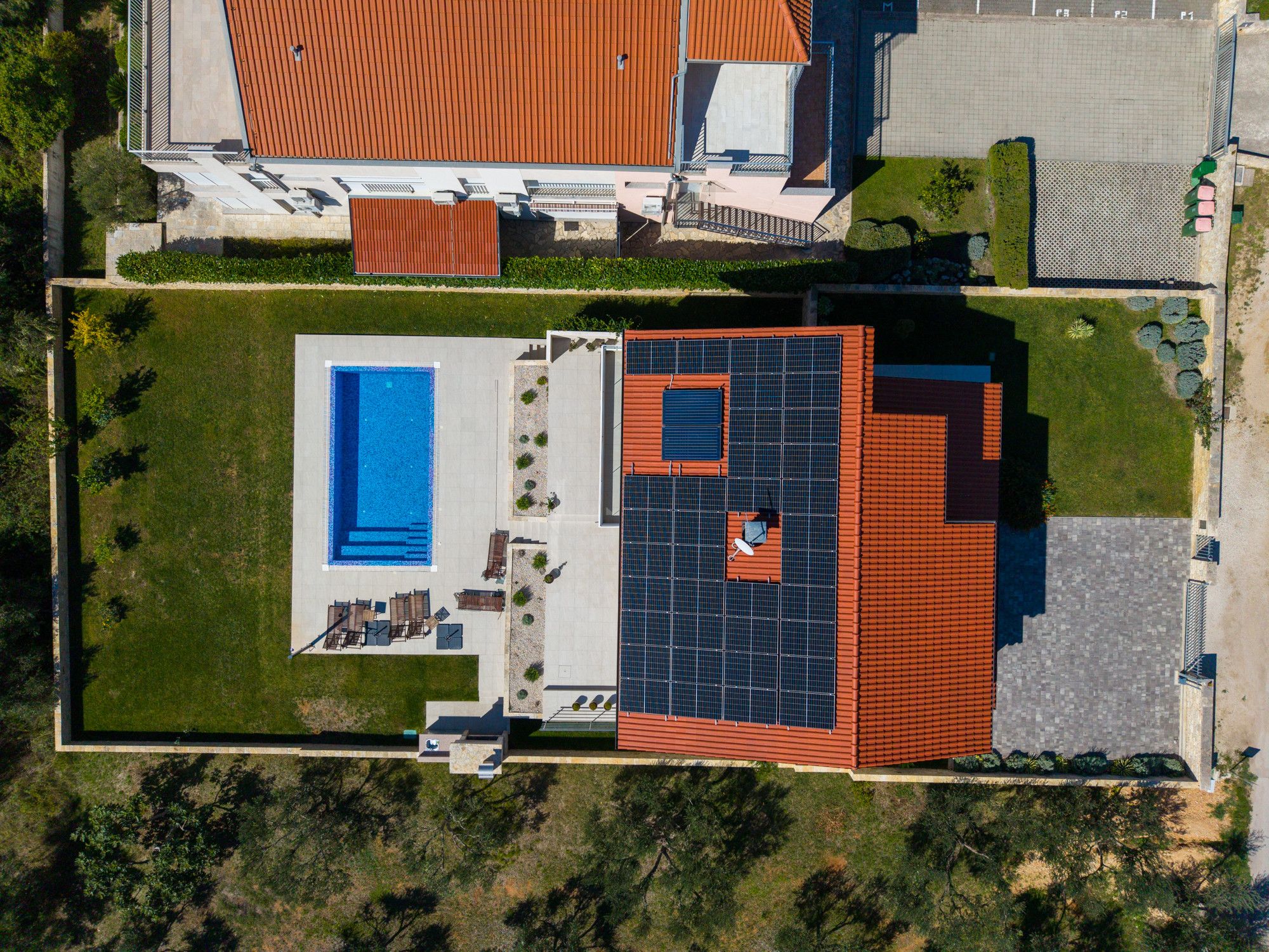 An aerial view of a property with a swimming pool, solar panels, and a large building with a red roof.