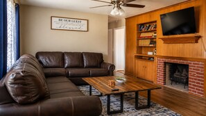 A living room with a leather sofa, a coffee table, a fireplace, a television, and a wall sign.