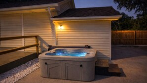Un jacuzzi frente a una casa con terraza de madera y una lámpara en la pared.