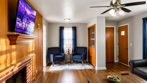 A living room with a fireplace, two armchairs, a coffee table, a TV, and a ceiling fan.