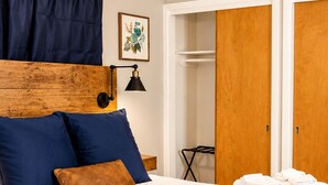 Una cama bien tendida con una manta y almohadas azules, un cabecero de madera, un ventilador de techo y un armario de madera.